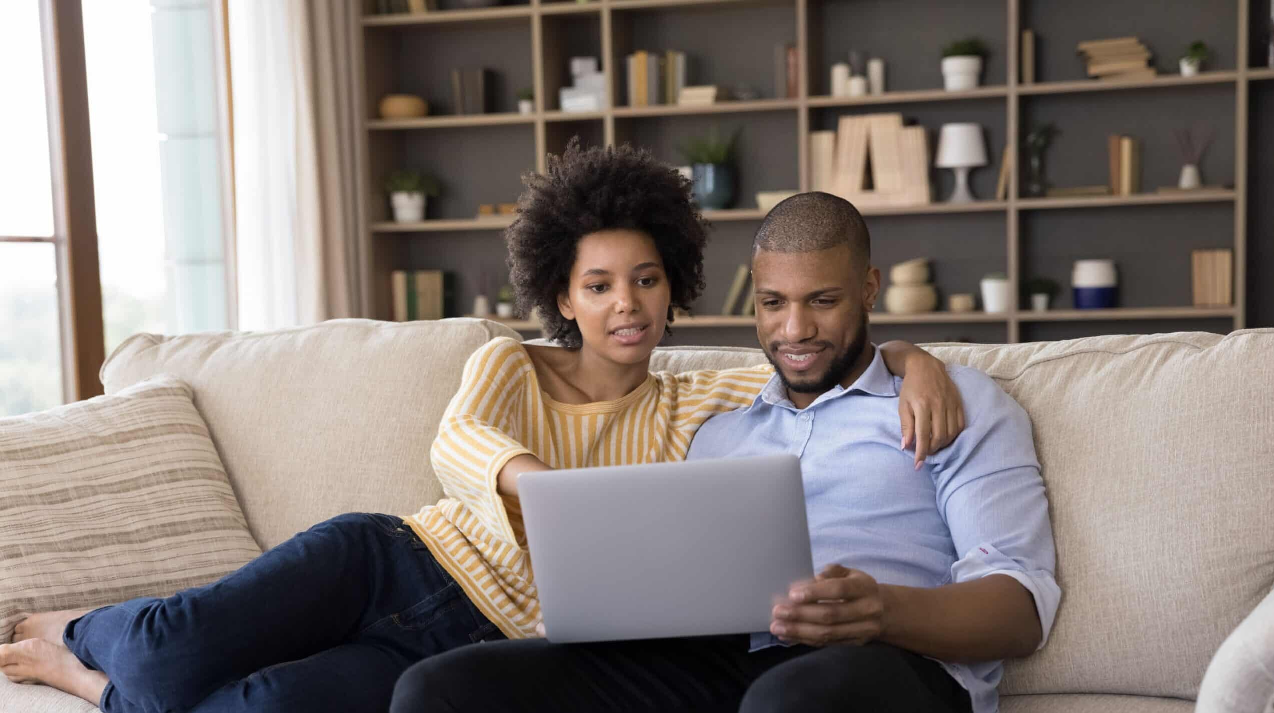 A young couple looking at a laptop while sitting on the couch in the home.