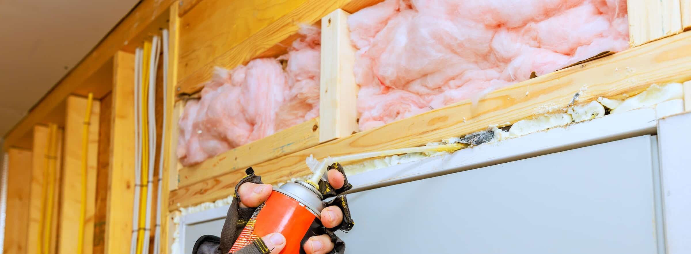 Hands applying caulk to air seal above a door. In the unfinished wall above the door is some pink fiberglass insulation.